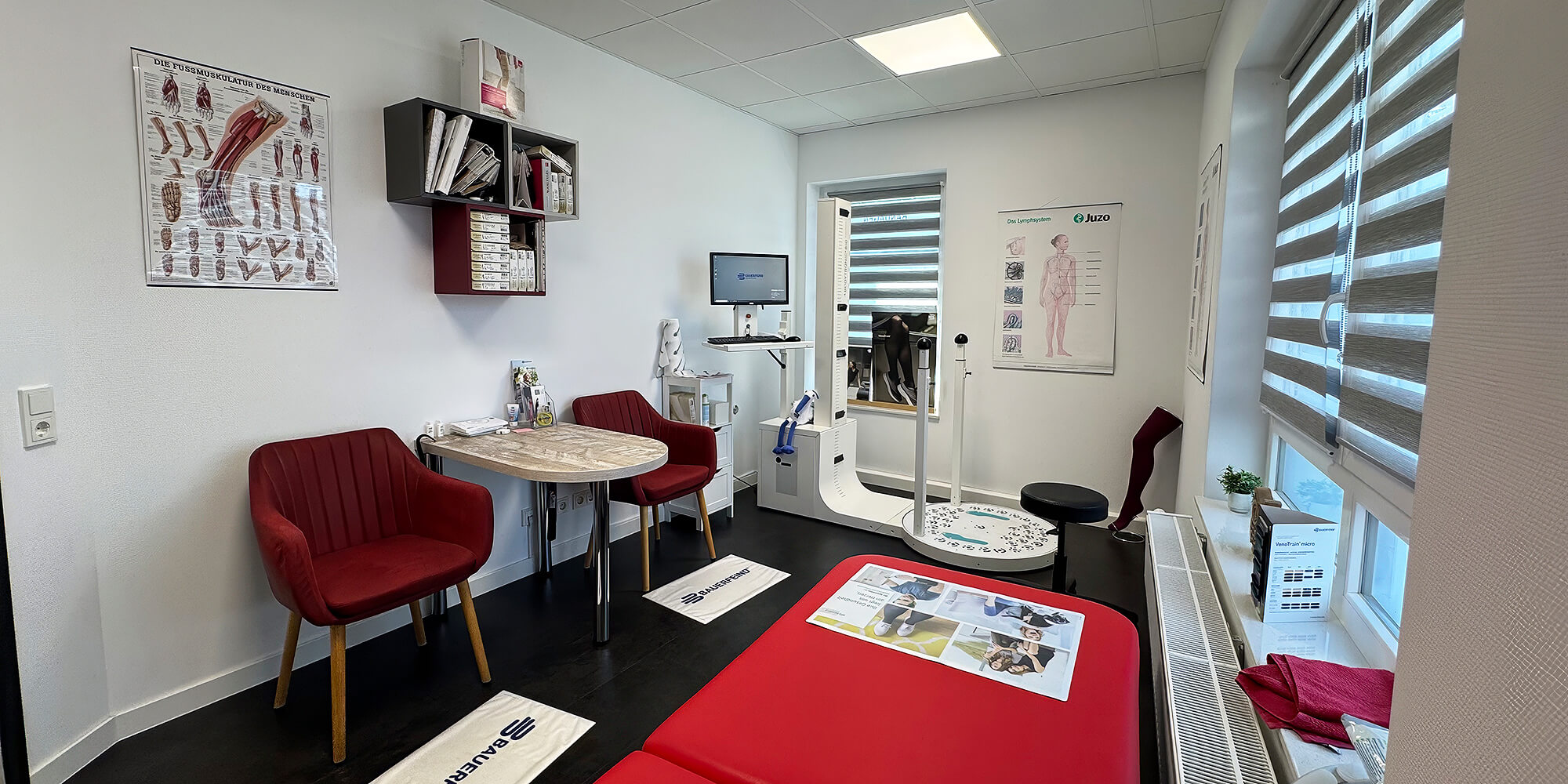 Moderner Behandlungsraum mit Sitzgruppe, roter Therapieliege und digitalem Messsystem für orthopädische Anpassungen